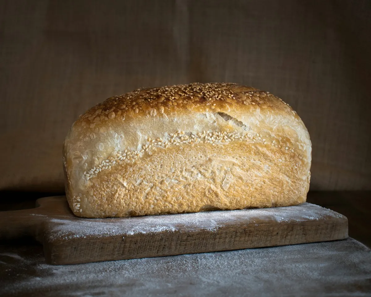 Sesame-topped sourdough loaf resting on a floured wooden board