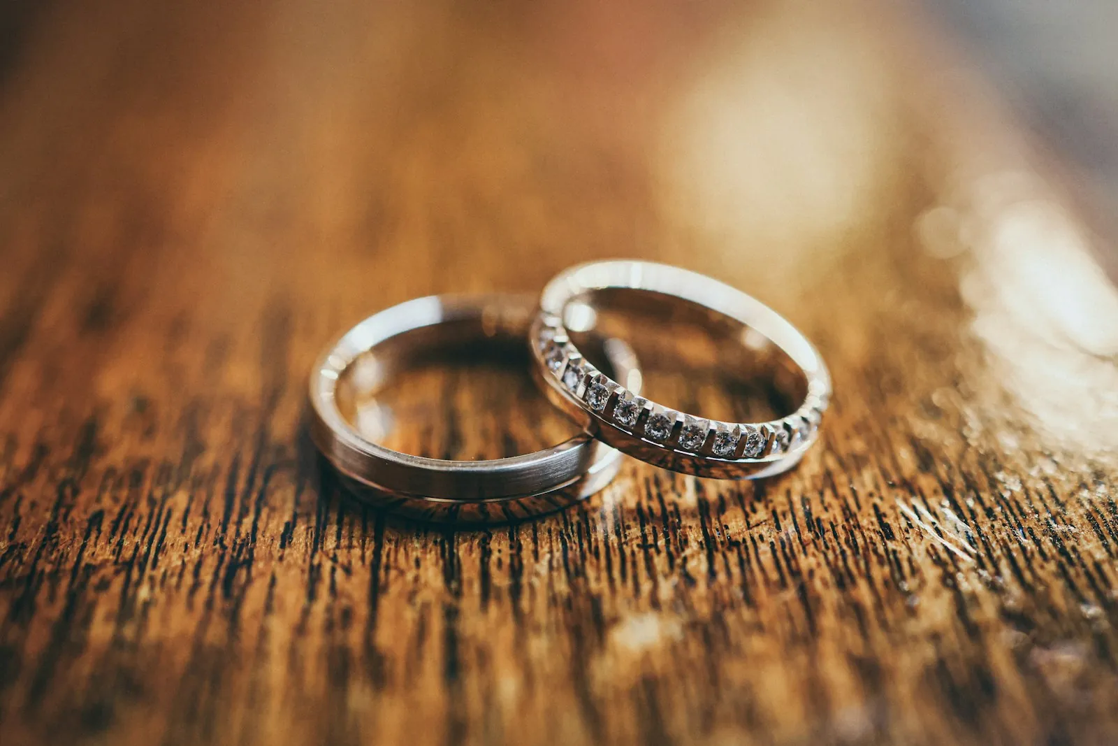 Two silver wedding bands, one set with small diamonds, rest together on a weathered wooden surface.