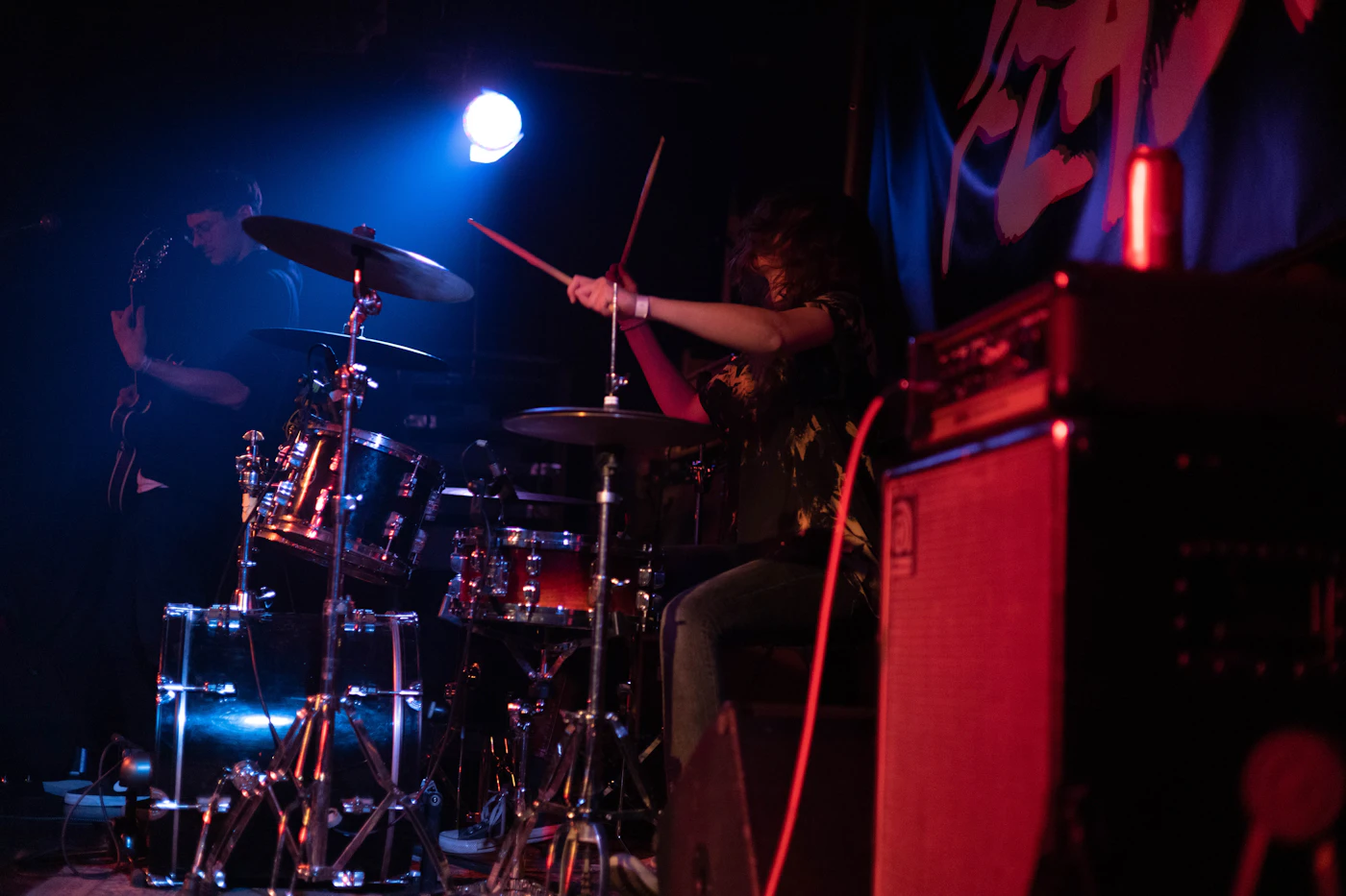 A drummer mid-song behind a drum kit under stage lights