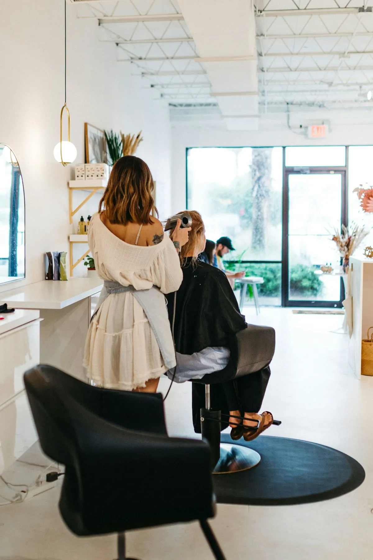Stylist blow-drying a client's hair near the front window