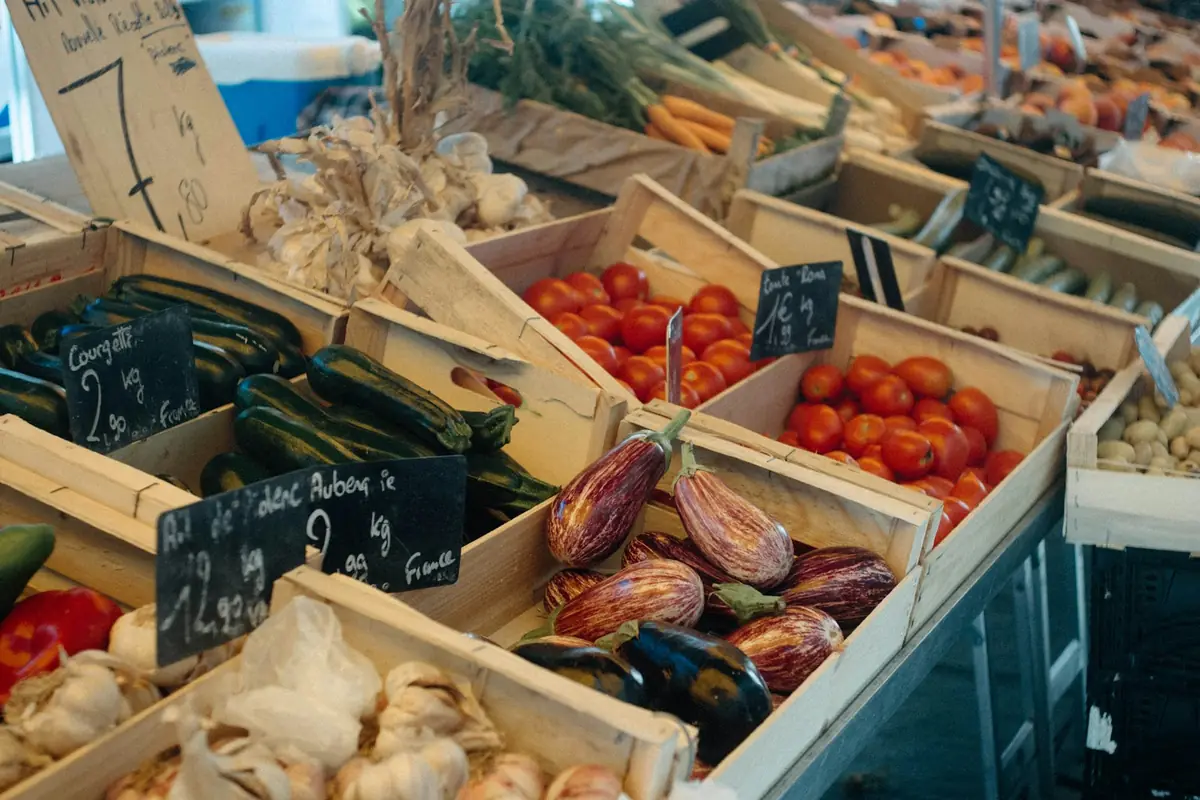 Wooden crates of zucchini, tomatoes, eggplant and garlic at a produce stand with handwritten price cards