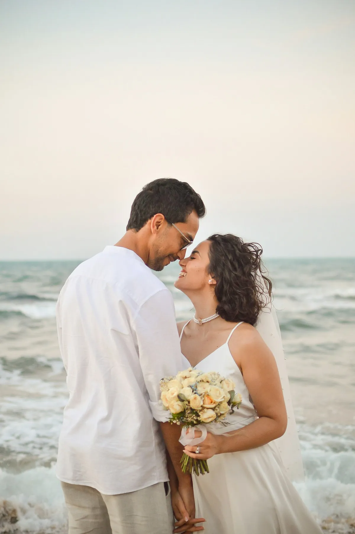 A bride and groom embracing and laughing on the beach