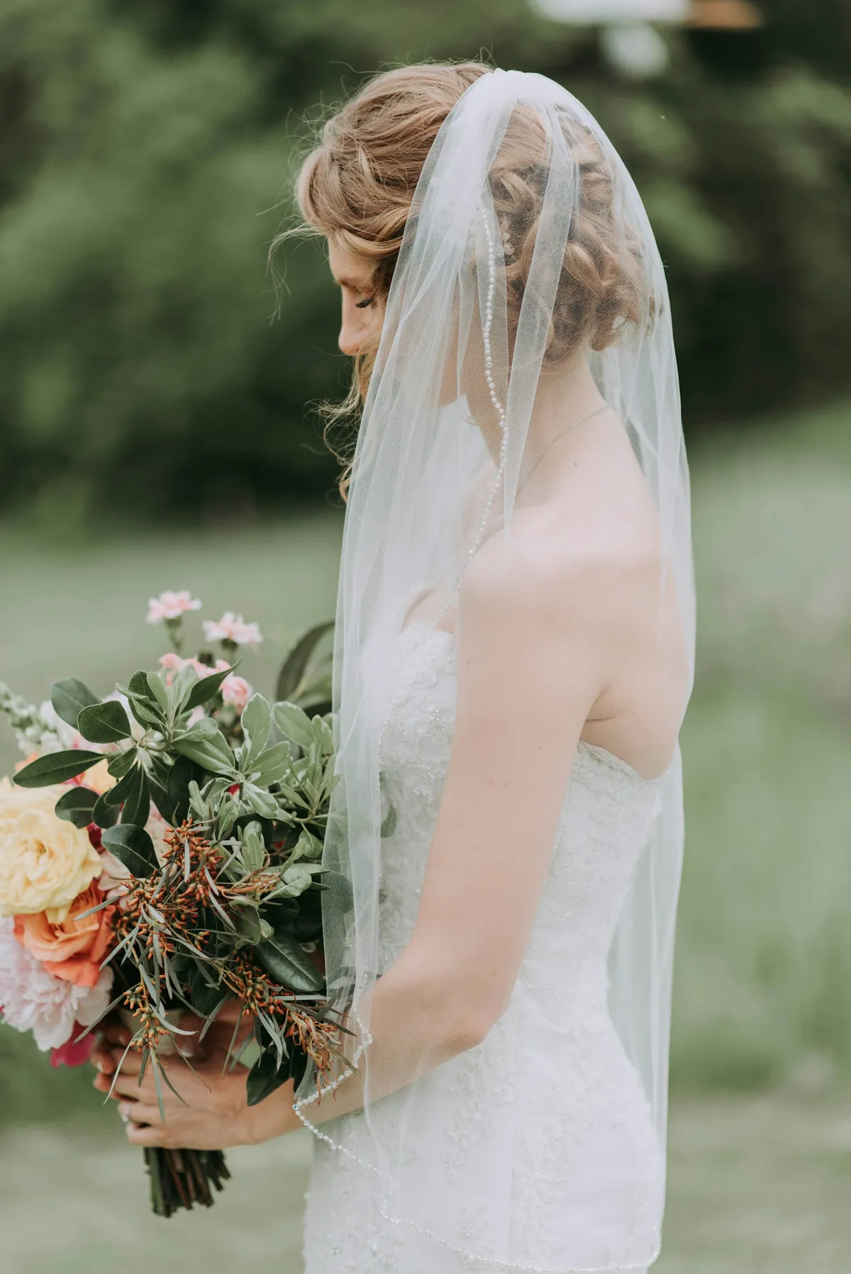 A bride in a lace gown and veil holding a wildflower bouquet