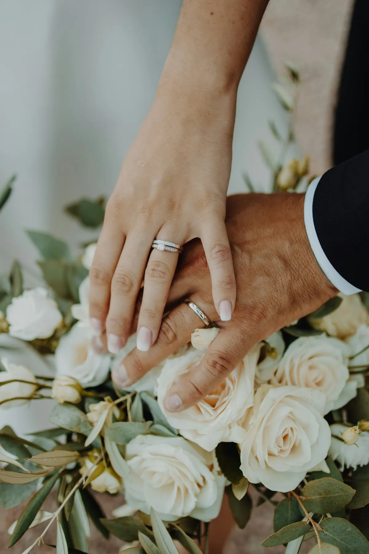 A couple's hands with wedding rings resting on white roses
