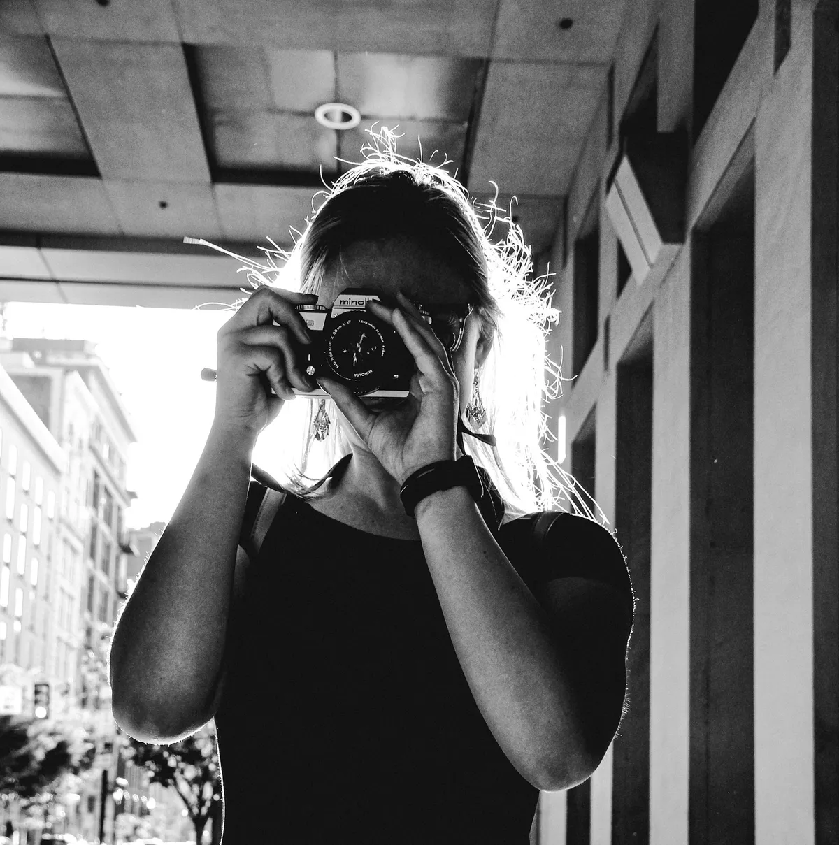 Black-and-white portrait of a photographer holding a film camera to her eye