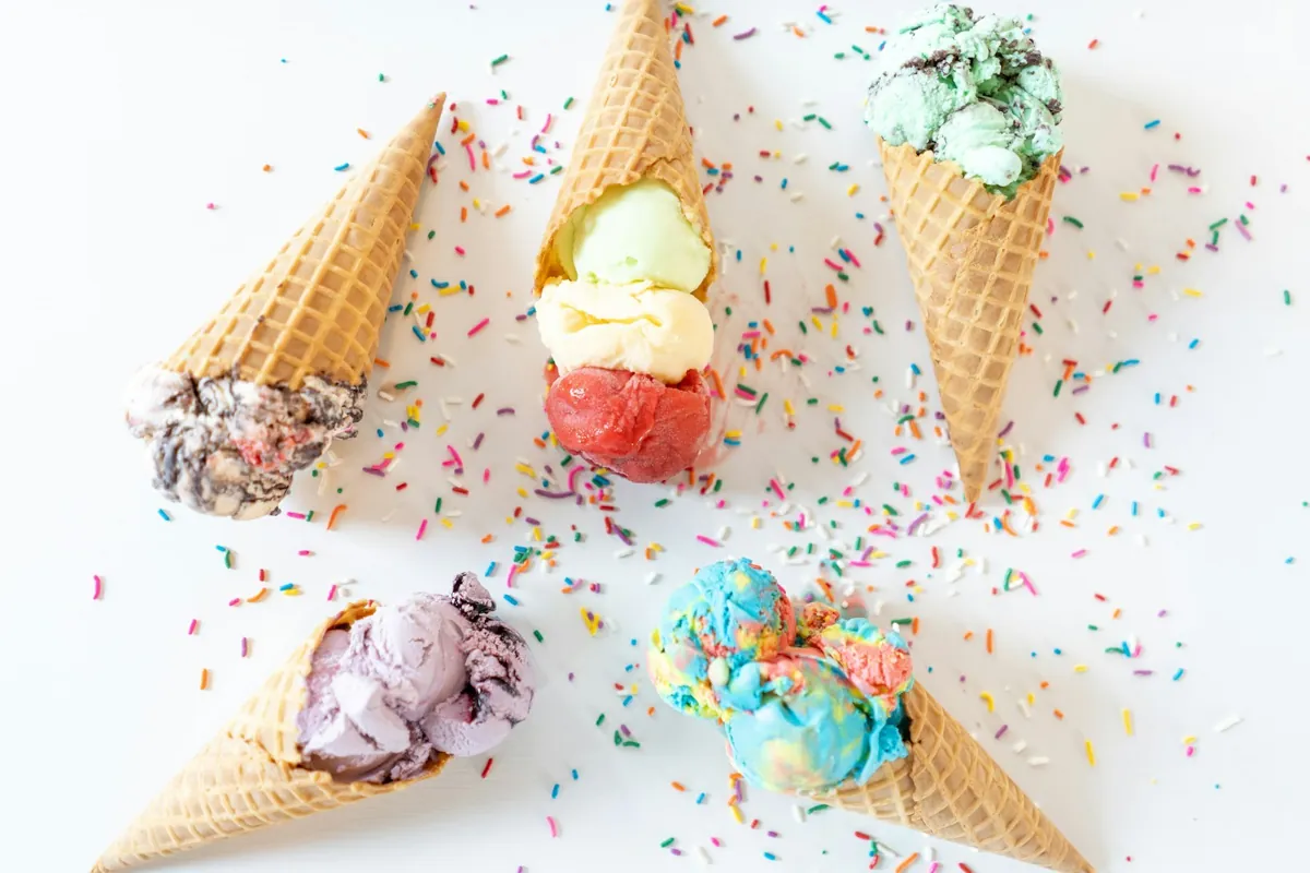 Five cones of different flavors lying on a table scattered with sprinkles