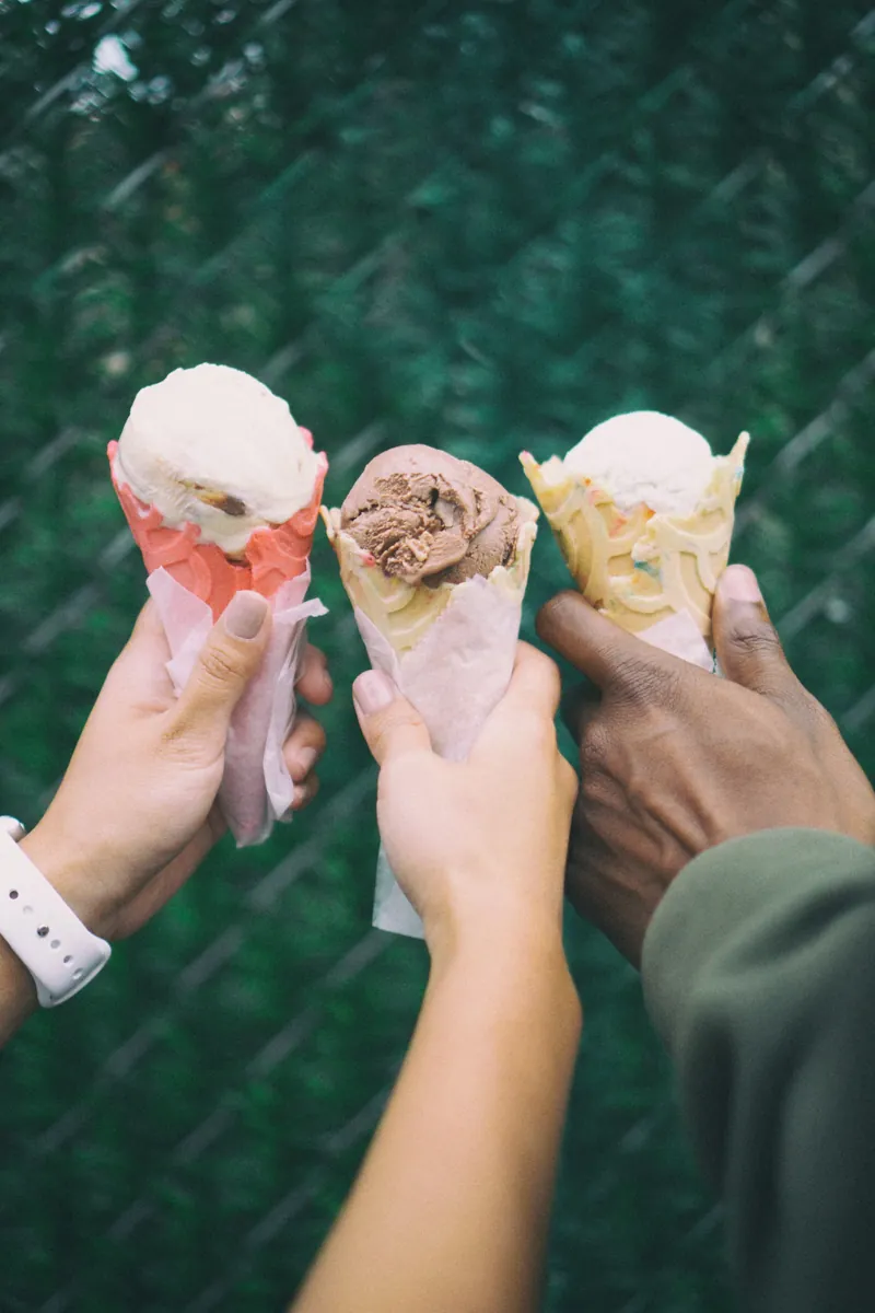 Three friends holding their cones together in front of a green hedge
