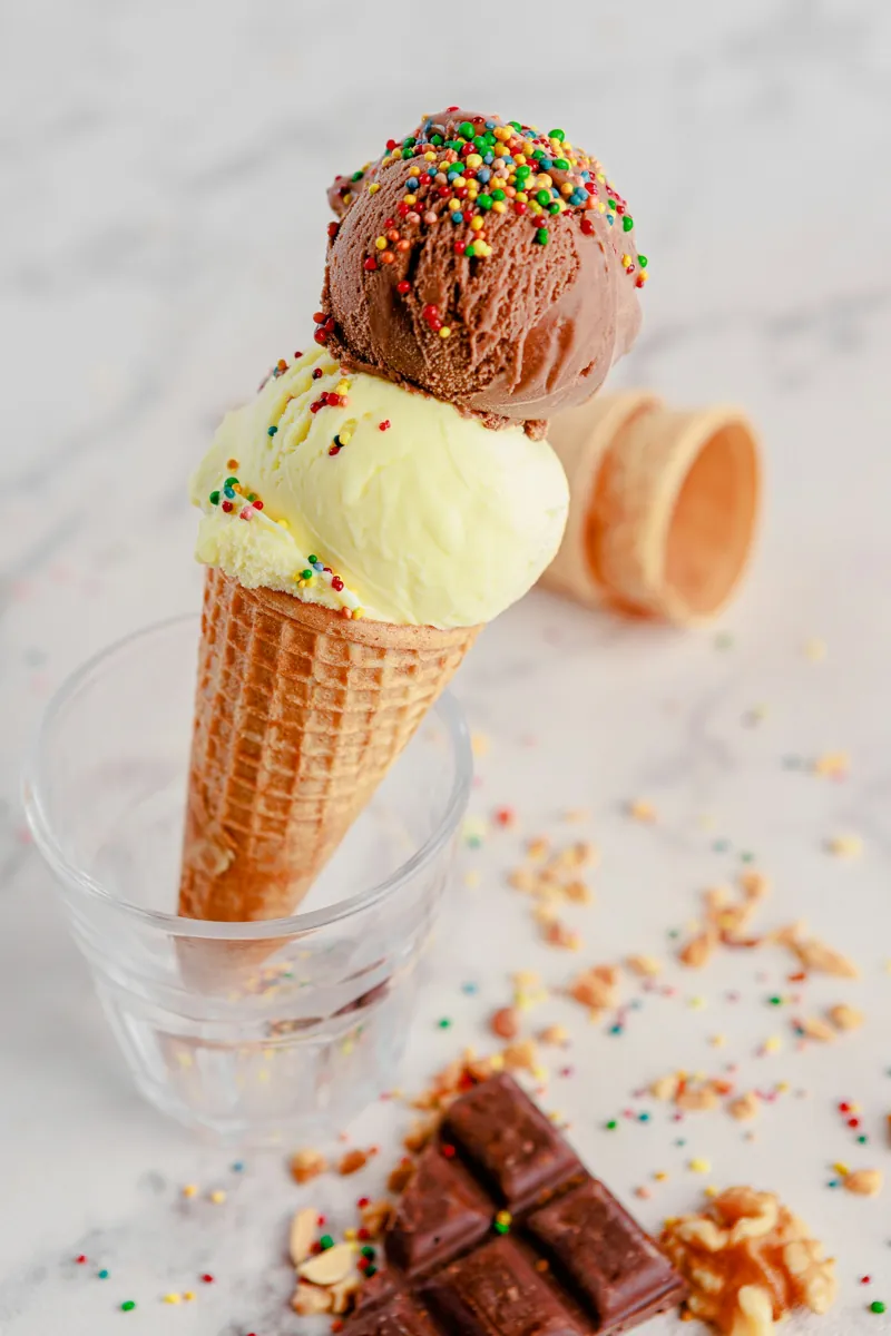 A chocolate scoop over a vanilla scoop with rainbow sprinkles in a waffle cone