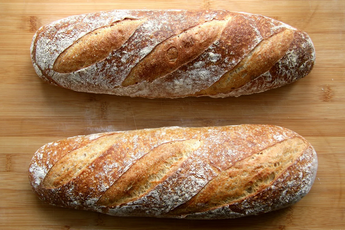 Two floured sourdough loaves with diagonal scoring on a wooden table