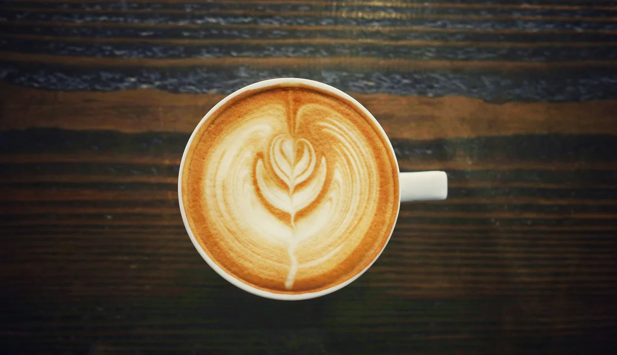 A cappuccino with leaf latte art in a white cup on a dark wood table