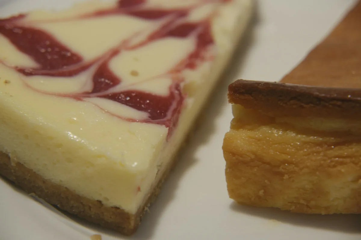 A slice of cheesecake with a red berry swirl beside a slice of tart